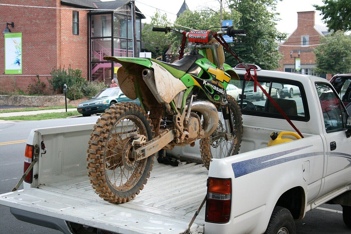 Moto de cross sanglée dans la benne d'un pick-up, sangles rouges visibles